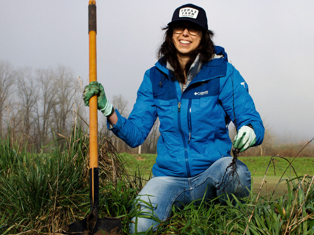 a young person holds a rake and kneels in the dirt